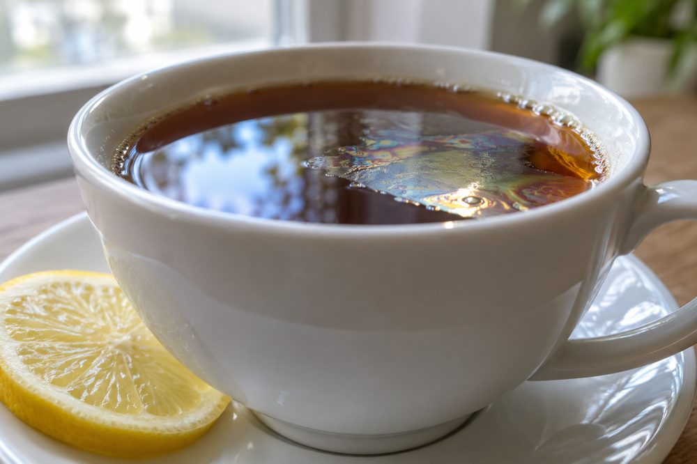 Close-up of a cup of black tea with a thin shiny film on the surface, next to a lemon slice